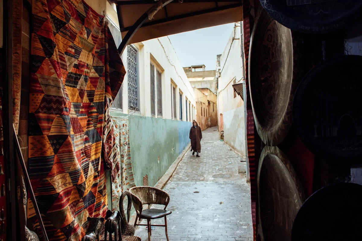 A person walks down a narrow alleyway with shops.