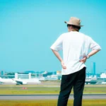 Man in hat at airport looks towards sky.