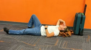 Exasperated Young man with suitcase lying on the floor waiting for his flight.